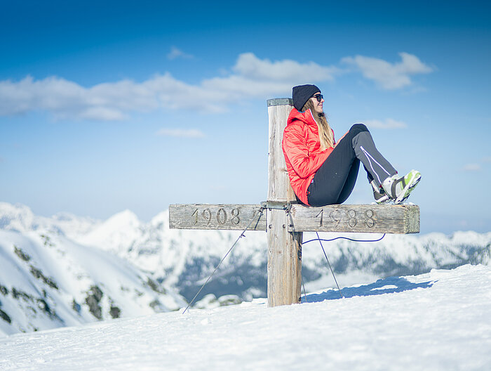 Eine Frau auf einem Gipfelkreuz in Obertauern