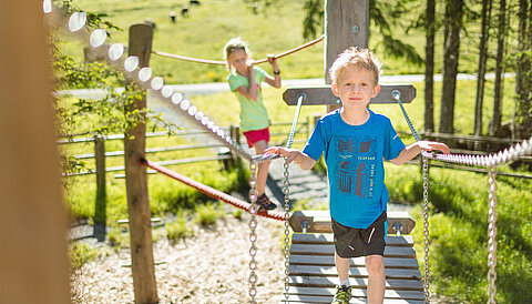 Zwei Kinder spielen auf dem Erlebnisweg Alles Alm