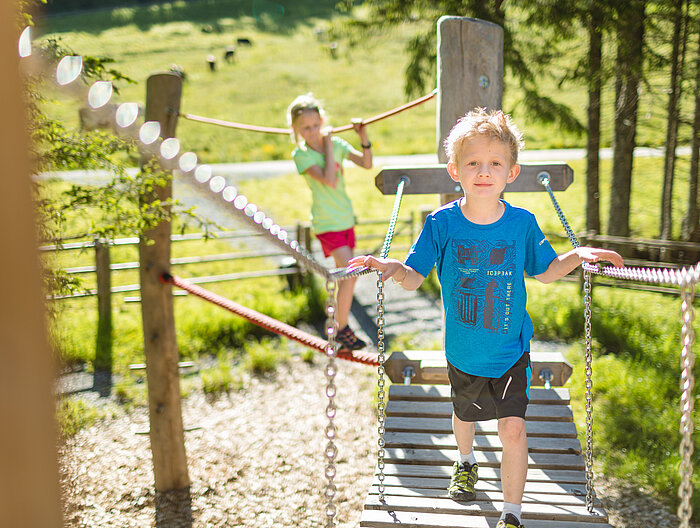 Zwei Kinder spielen auf dem Erlebnisweg Alles Alm