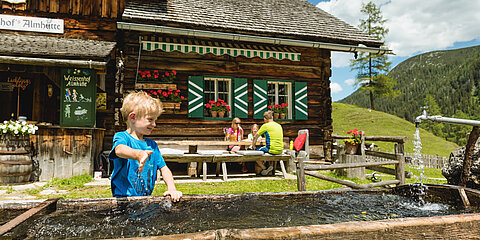 Ein Junge spielt am Brunnen der Weissenhof Almhütte