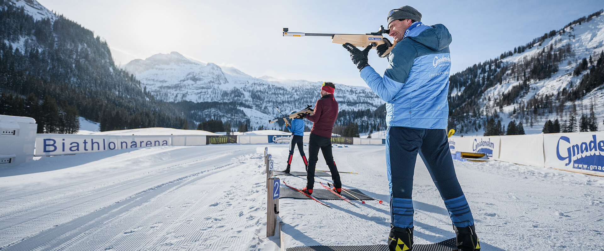 Drei Personen beim Zielen mit einer Biathlonwaffer vor der Gnadenalm